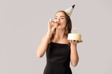 Gri arka planda parti düdüğü ve tatlı pastayla doğum gününü kutlayan güzel genç bir kadın.