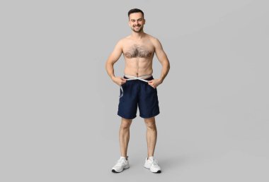 Gri arka planda belini ölçen yakışıklı, genç bir adam. Kilo verme konsepti