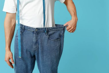 Mavi arka planda şeridi olan bol kotlu yakışıklı genç adam, yakın plan. Kilo verme konsepti