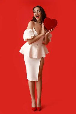 Kırmızı arka planda kalp şeklinde hediye kutusu olan mutlu genç bir kadın.