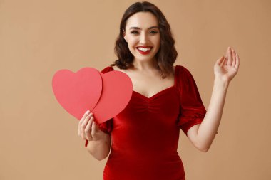 Kahverengi arka planda kırmızı kağıt kalpleri olan güzel genç bir kadın.