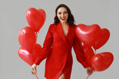 Gri arka planda kalp şeklinde hava balonları olan genç bir kadın.