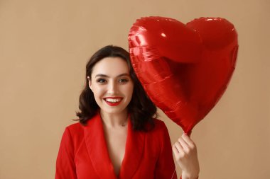 Kahverengi arka planda kalp şeklinde hava balonu olan güzel genç bir kadın.