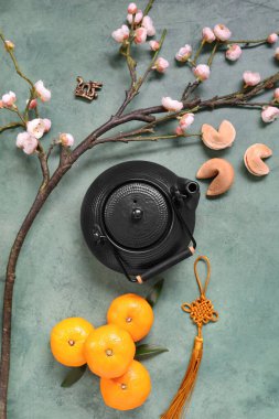 Sakura dalı çaydanlık, mandalina ve fal kurabiyeleri ile gri grunge arka planda. Yeni yıl kutlaması