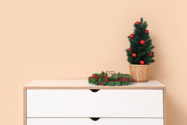 İçinde Noel ağacı olan bir elbise ve bej duvarın yanında çelenk.