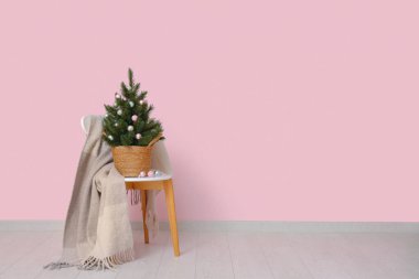Tencerede Noel ağacı ve pembe duvarın yanında ekoseli sandalye.