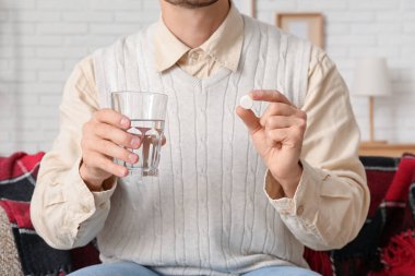Bir bardak su ve hapla evde oturan hasta genç adam, yakın plan.