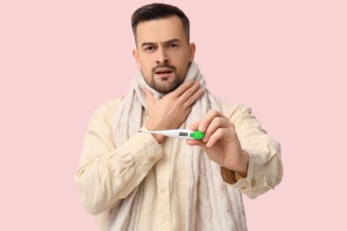 Pembe arka planda termometresi olan hasta genç bir adam.