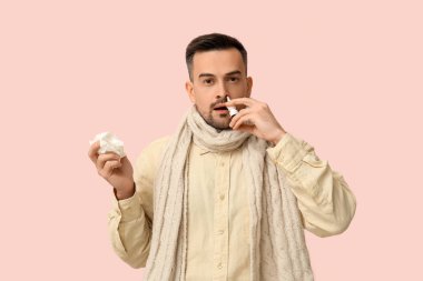 Pembe arka planda burun damlası kullanan dokuları olan hasta genç bir adam.