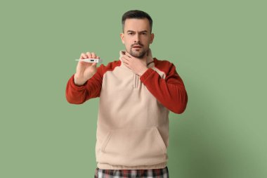 Yeşil arka planda termometresi olan hasta genç bir adam.