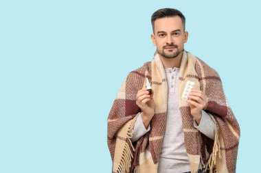 Burun damlası ve mavi arka planda hapları olan hasta genç bir adam.