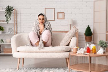 Evdeki kanepede oturan ekoseli hasta genç kadın.