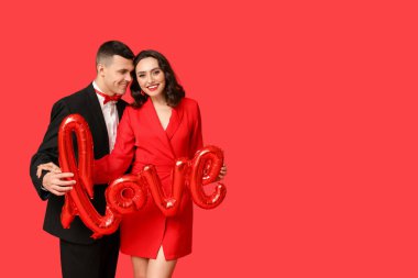 Kırmızı arka planda aşk kelimesi şeklinde balonları olan sevgi dolu genç bir çift. Sevgililer Günü 'nün kutlaması