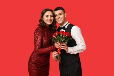 Kırmızı arka planda bir buket güzel gülleri olan sevimli genç bir çift. Sevgililer Günü 'nün kutlaması