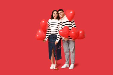 Kırmızı arka planda kalp şeklinde balonları olan sevgi dolu genç bir çift. Sevgililer Günü 'nün kutlaması