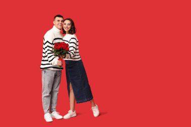 Kırmızı arka planda bir buket güzel gülleri olan sevimli genç bir çift. Sevgililer Günü 'nün kutlaması