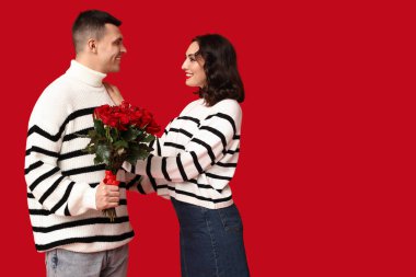 Kırmızı arka planda bir buket güzel gülleri olan sevimli genç bir çift. Sevgililer Günü 'nün kutlaması