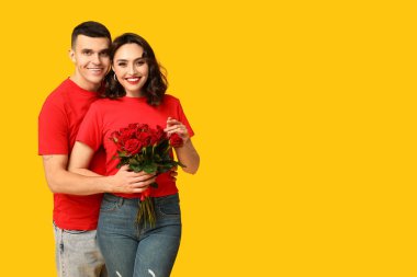 Sarı arka planda bir buket güzel gülleri olan sevimli genç bir çift. Sevgililer Günü 'nün kutlaması