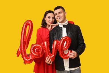 Sarı arka planda aşk kelimesi şeklinde balonları olan sevgi dolu genç bir çift. Sevgililer Günü 'nün kutlaması