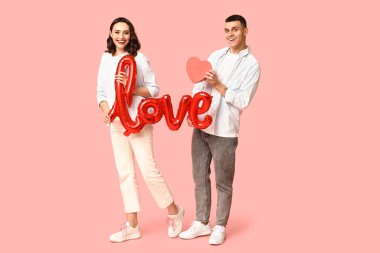 Aşk kelimesi şeklinde balonu ve pembe arka planda kağıt kalbi olan sevimli genç bir çift. Sevgililer Günü 'nün kutlaması