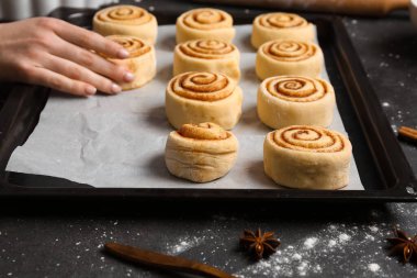 Woman preparing cinnamon rolls at table clipart