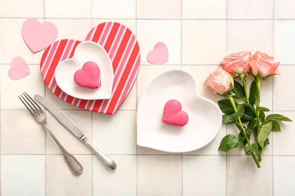 Beautiful table setting with roses and cakes for Valentine\'s Day on white tile background