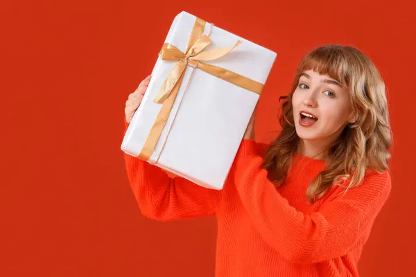Beautiful shocked young woman with gift box on orange background