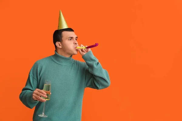 Young man in party hat with glass of champagne celebrating Christmas on orange background