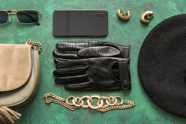 Set of stylish female accessories with leather gloves and modern mobile phone on green background