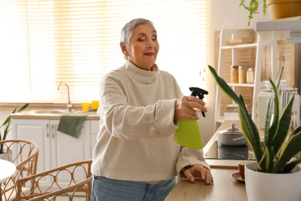 stock image Senior woman watering plant in kitchen