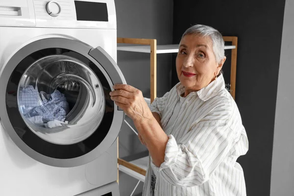 Senior woman with washing machine in laundry room