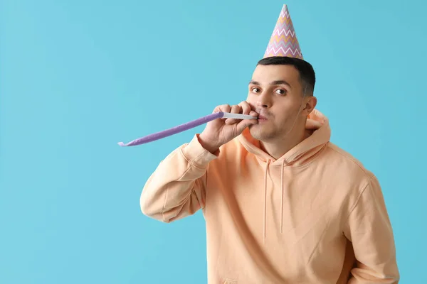 Young man in Birthday hat with with party whistle on blue background