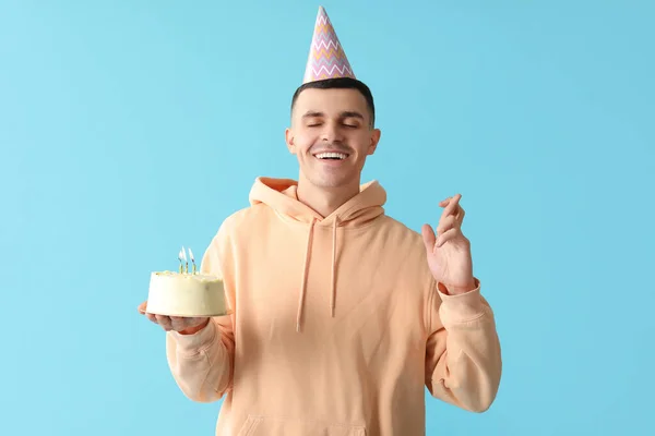 Young man in party hat with sweet cake on blue background