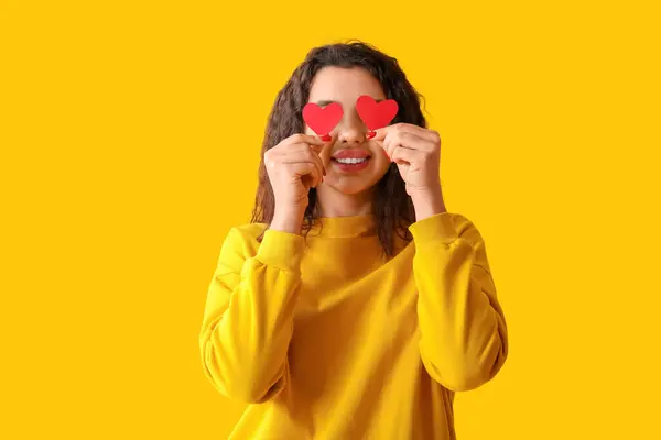 黄色の背景に赤い紙の心を持つ美しい若い女性 — ストック写真