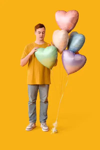 Young man with heart shaped air balloons on yellow background