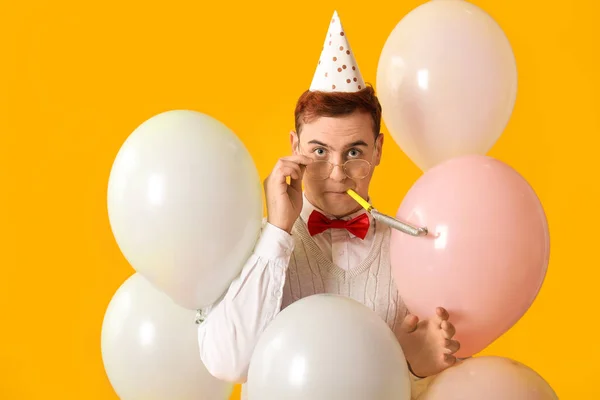 Young man with party whistle and air balloons celebrating Birthday on yellow background