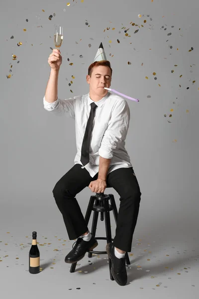 Young man with party whistle and glass of champagne celebrating Birthday on grey background