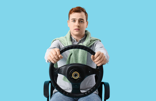 Young man with steering wheel on blue background