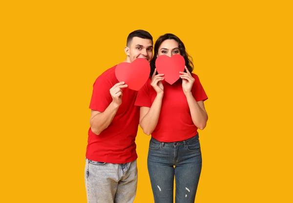 Loving young couple with paper hearts on yellow background. Celebration of Saint Valentine's Day