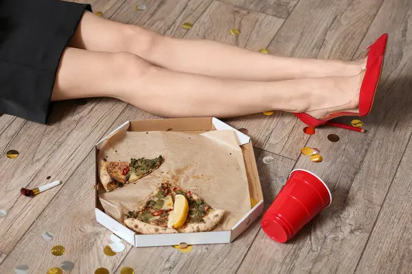 Drunk woman with pizza leftovers and cup in office after New Year party, closeup