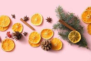 Köknar dallı kurutulmuş portakal dilimleri, tarçın, yıldız anason ve pembe arka planda çam kozalakları.