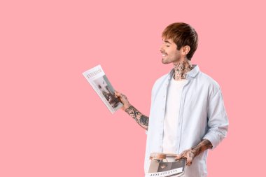 Pembe arka planda iç dergisi olan dövmeli genç adam.