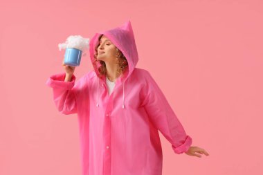 Pembe arka planda bulutlu yağmurluk giyen genç bir kadın.