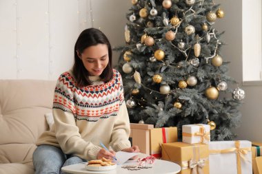 Güzel genç bayan evde Noel kutlaması için tebrik kartı yazıyor.