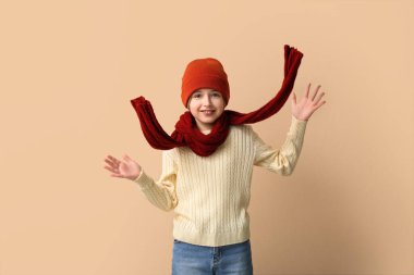 Bej arka planda kışlık giysiler içinde şirin, mutlu bir çocuk.