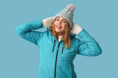 Mavi arka planda sıcak kış giysileri içinde güzel, genç, mutlu bir kadın.