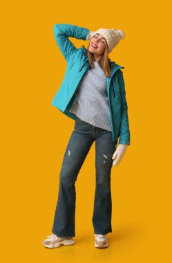 Sarı arka planda sıcak kış giysileri içinde güzel, genç ve mutlu bir kadın.