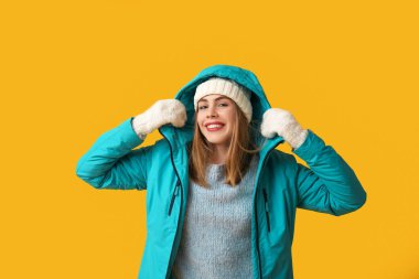 Sarı arka planda sıcak kış giysileri içinde güzel, genç ve mutlu bir kadın.