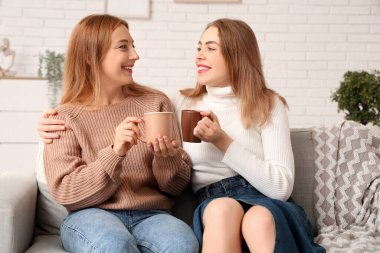 Evdeki kanepede annesine bir fincan sıcak kahveyle sarılan güzel bir genç kadın. Uluslararası Sarılma Günü