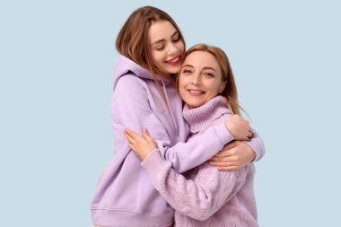 Mavi arka planda annesine sarılan mutlu genç bir kadın. Uluslararası Sarılma Günü